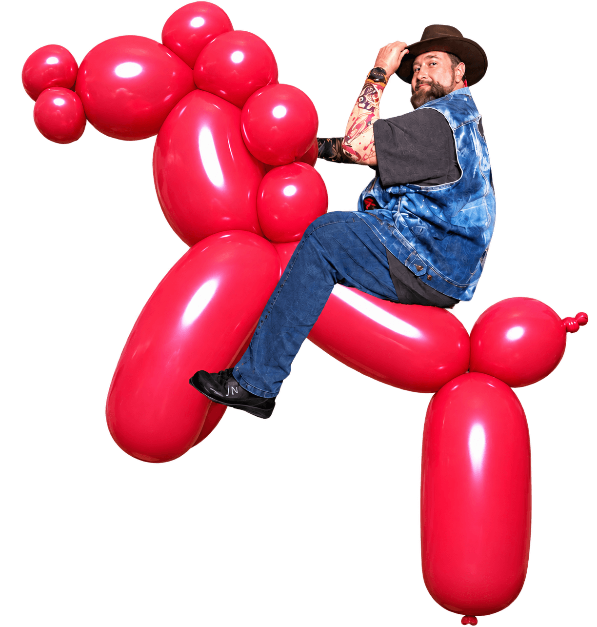 Kevin Skelling in a cowboy hat and denim vest, tipping his hat while perched on an enormous red balloon horse